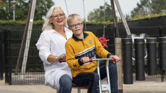 Twee mensen rijden op een tandemdriewieler, waarbij de persoon vooraan stuurt en trapt, en de persoon achteraan zit en zich vasthoudt.