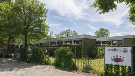 Vooraanzicht van dagbestedingslocatie Noorderkroonstraat in Dordrecht, met tuin en toegangshek.