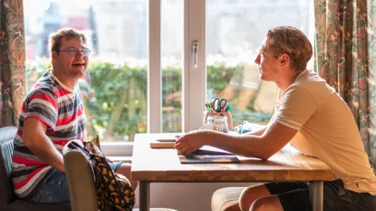 Twee mensen zitten tegenover elkaar aan een tafel met een pot gekleurde pennen