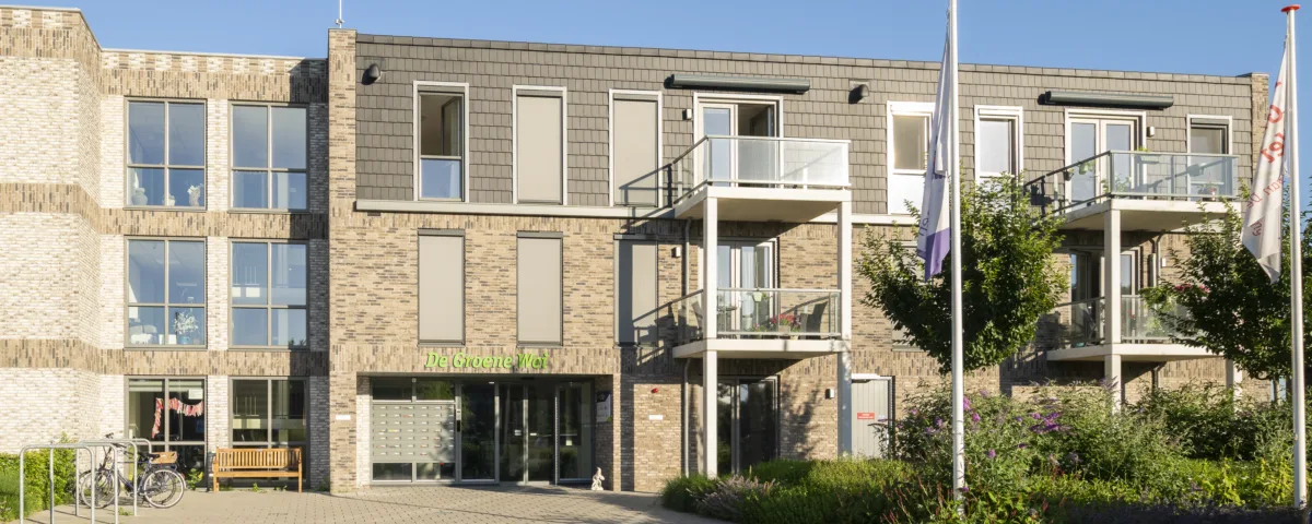 Vooraanzicht van woonlocatie De Groene Wei in Giessenburg met centrale entree, balkons en groene beplanting.
