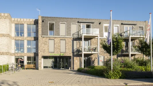 Vooraanzicht van woonlocatie De Groene Wei in Giessenburg met centrale entree, balkons en groene beplanting.