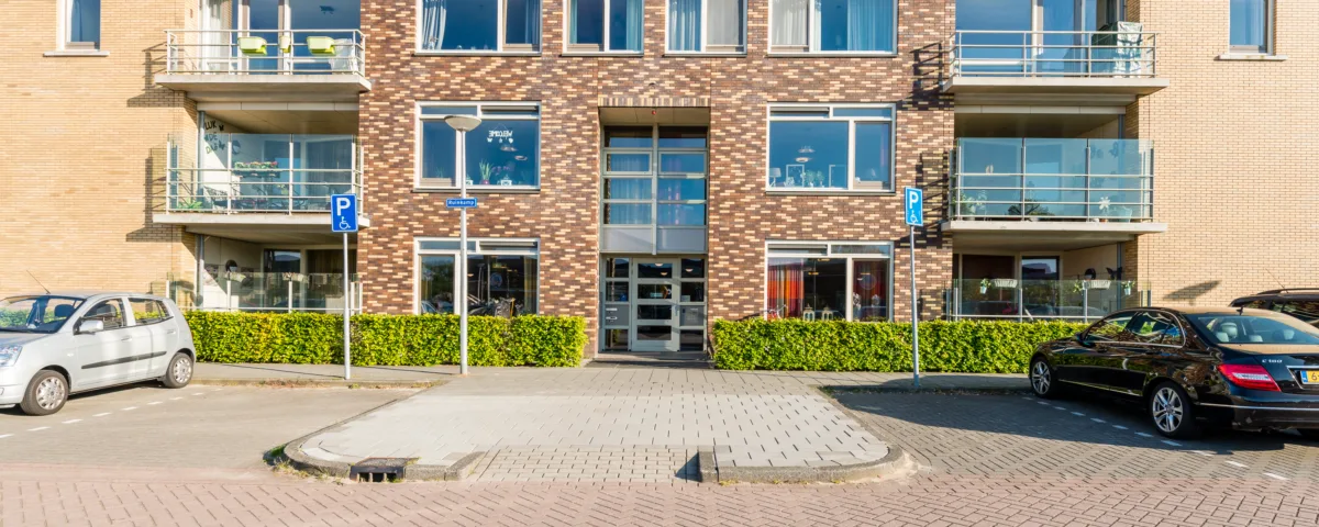 Modern appartementencomplex met drie verdiepingen, balkons en geparkeerde auto's ervoor