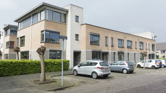 Een moderne woonstraat met aaneengesloten huizen met grote ramen en een mix van bakstenen en witte gevels. Er staan meerdere auto's geparkeerd voor de huizen en een straatbord met de naam "Stierstraat"