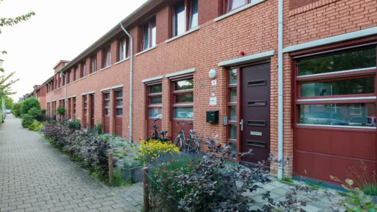 Rij van moderne, rode bakstenen huizen met grote ramen, donkerbruine deuren, fietsen en plantenbakken langs het trottoir