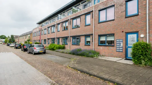 Rij moderne, meer verdiepingen tellende bakstenen herenhuizen met grote ramen, balkons met groen en geparkeerde auto's