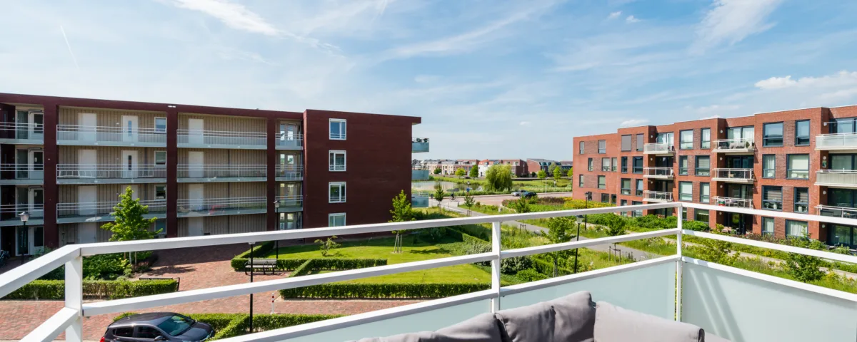Uitzicht vanaf een balkon met een comfortabele buitenbank, moderne appartementen, groene gazons en bomen